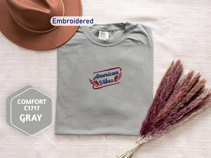 a gray t-shirt with a red and blue logo, a brown hat, and some purple flowers on a white background.