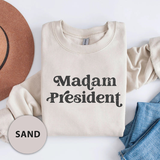 a white shirt that says madam president next to a hat