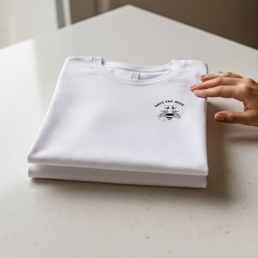 A white t-shirt with the text "SAVE THE BEES" printed on it, along with a bee graphic, is being held by a person's hand.