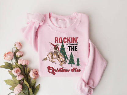 A pink sweatshirt with a graphic design featuring a cowboy riding a bucking bronco, surrounded by Christmas trees and flowers.