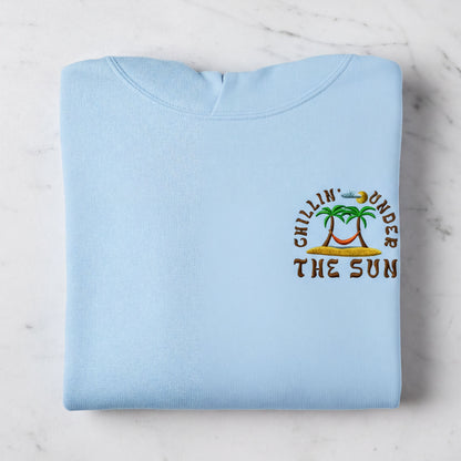 A light blue hoodie with an embroidered design on the right side, depicting a palm tree and the text "Chillin' under the sun".