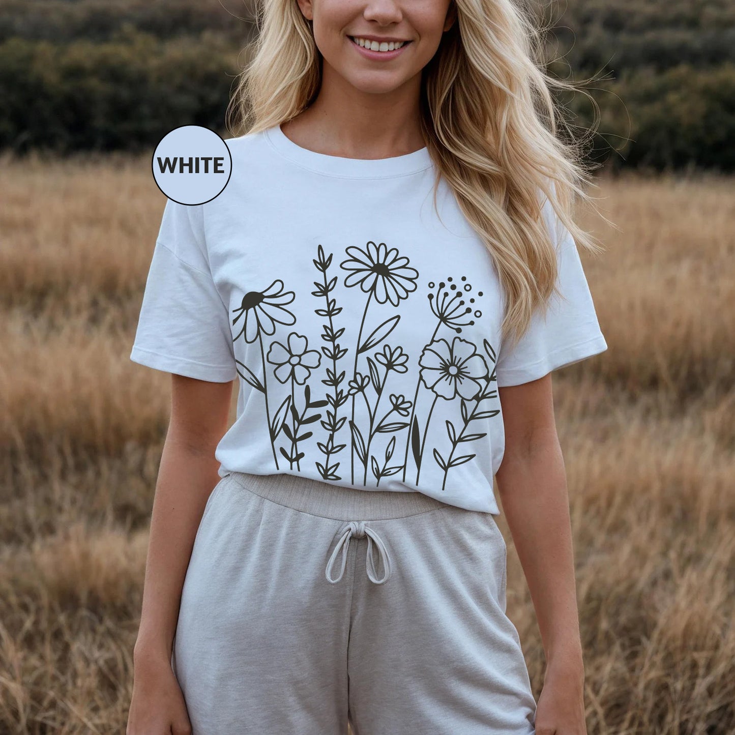 a woman standing in a field wearing a t - shirt with flowers on it