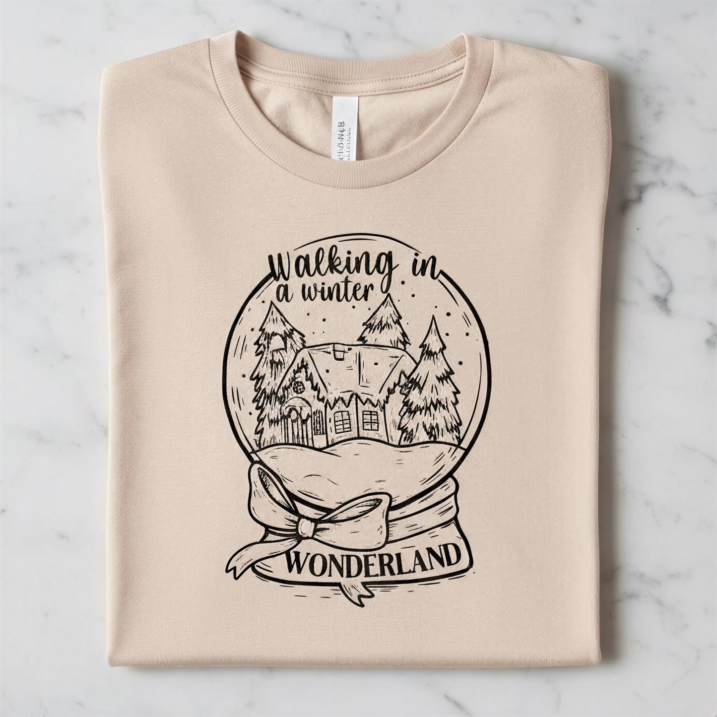A t-shirt with a graphic design depicting a snow globe containing a winter scene with a house and trees, along with the text "Walking in winter wonderland".