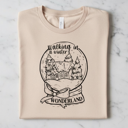 A t-shirt with a graphic design depicting a snow globe containing a winter scene with a house and trees, along with the text "Walking in winter wonderland".