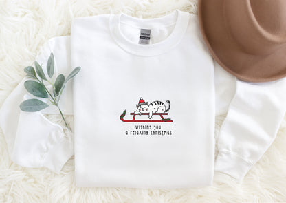 A white long-sleeved t-shirt with a graphic design of a cat wearing a Santa hat and the text "Wishes you a relaxing christmas" printed on it, along with a brown hat and a sprig of greenery.