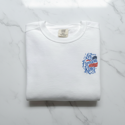 A white t-shirt with a blue and red design on the left side, featuring the text "Let Freedom Ring" in a stylized font.