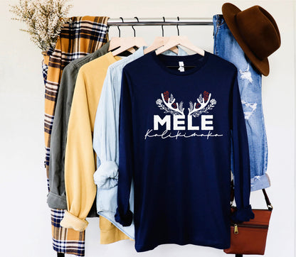 A clothing rack displaying various items, including a navy blue long-sleeve shirt with the text "MELE KALIKINMAK" printed on it, a plaid shirt, a yellow shirt, and a pair of blue jeans.