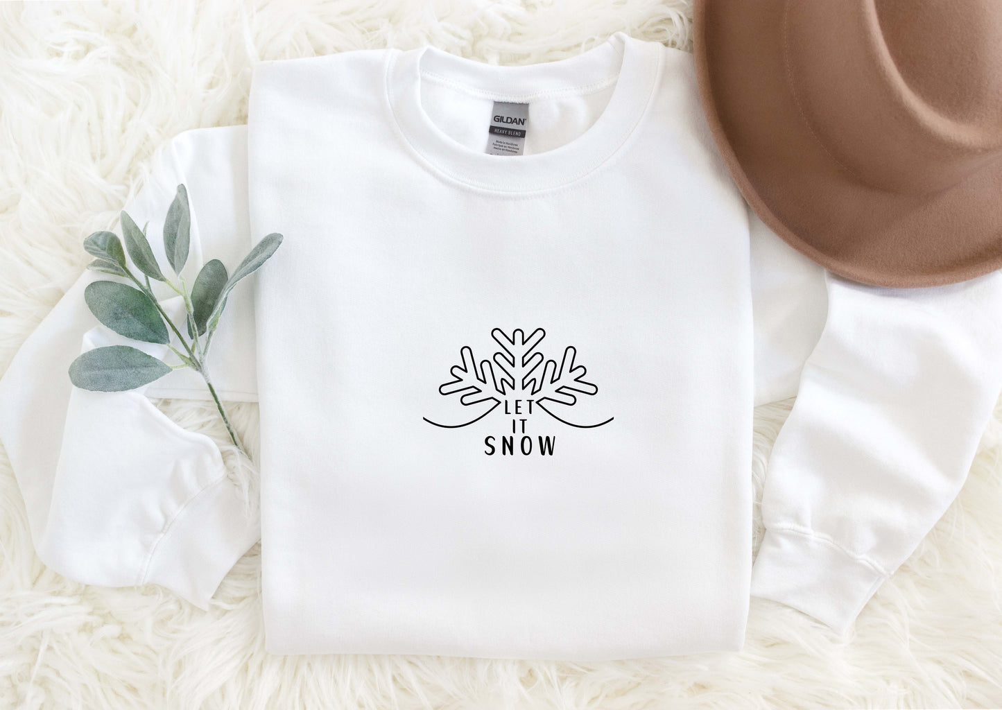 A white long-sleeved shirt with a black graphic design and text, along with a brown hat, a green plant, and a white furry surface.