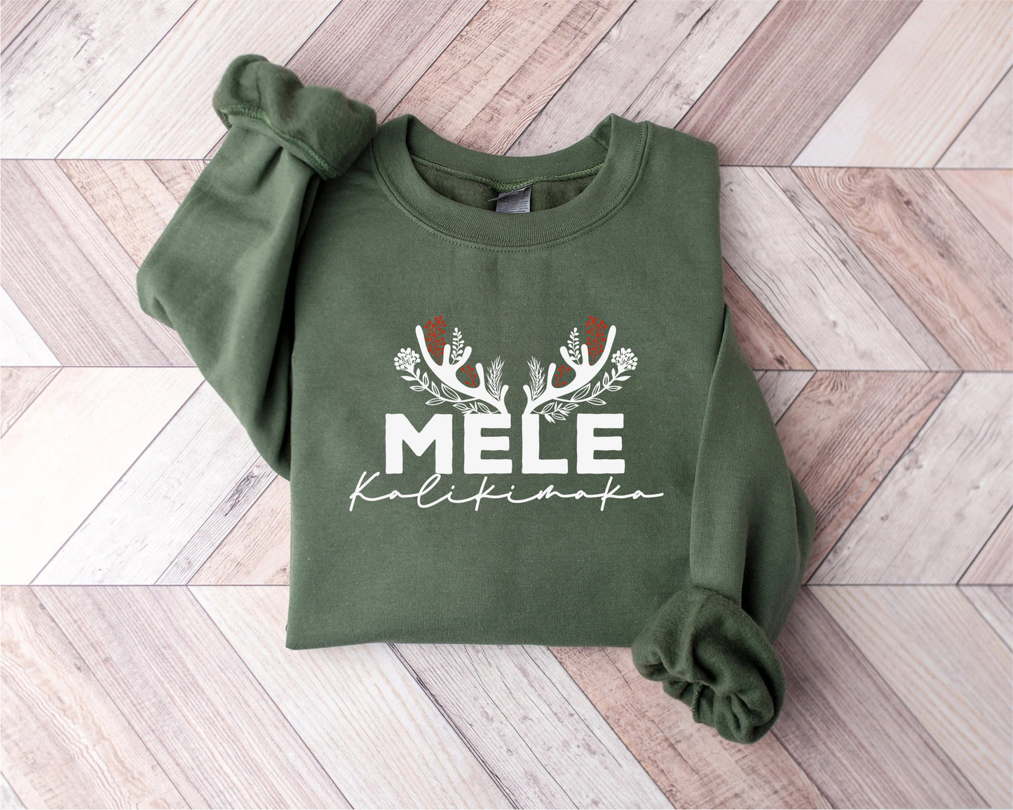 A green sweatshirt with the text "MELE KOLIKINAKA" printed on it, along with a decorative design featuring antlers and flowers.