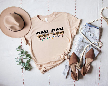a casual outfit consisting of a beige t-shirt with a graphic design, a beige hat, a pair of jeans, and brown shoes, all laid out on a white background.