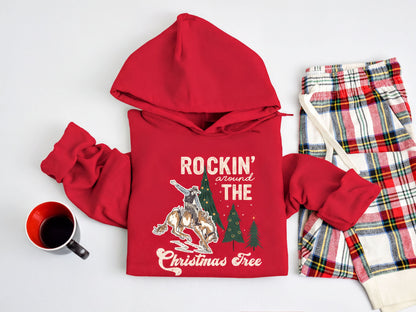 A red hoodie with a Christmas tree design and the text "ROCKIN' around THE CHRISTMAS Tree" is displayed on a white background, along with a pair of plaid pajama pants and a mug.