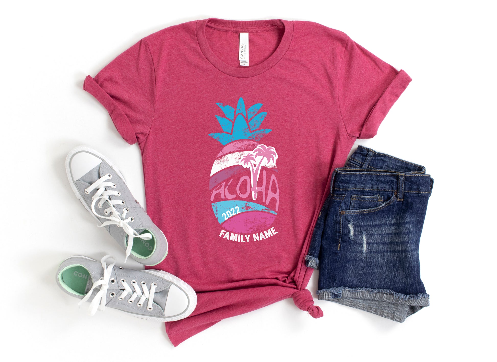 A red t-shirt with a graphic design, a pair of gray sneakers, and a pair of denim shorts are laid out on a white background.