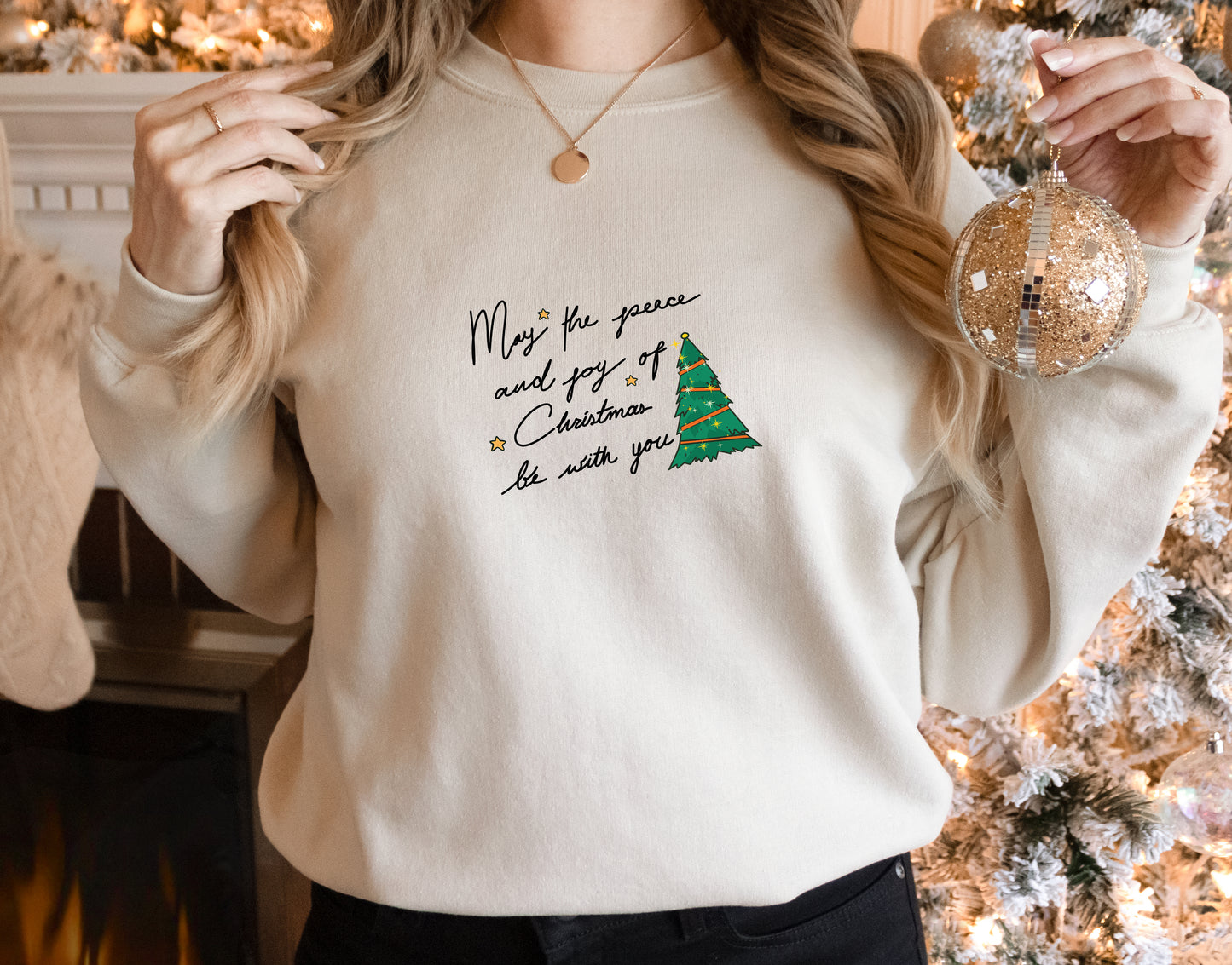 A woman wearing a white sweater with a Christmas-themed design and holding a Christmas ornament.