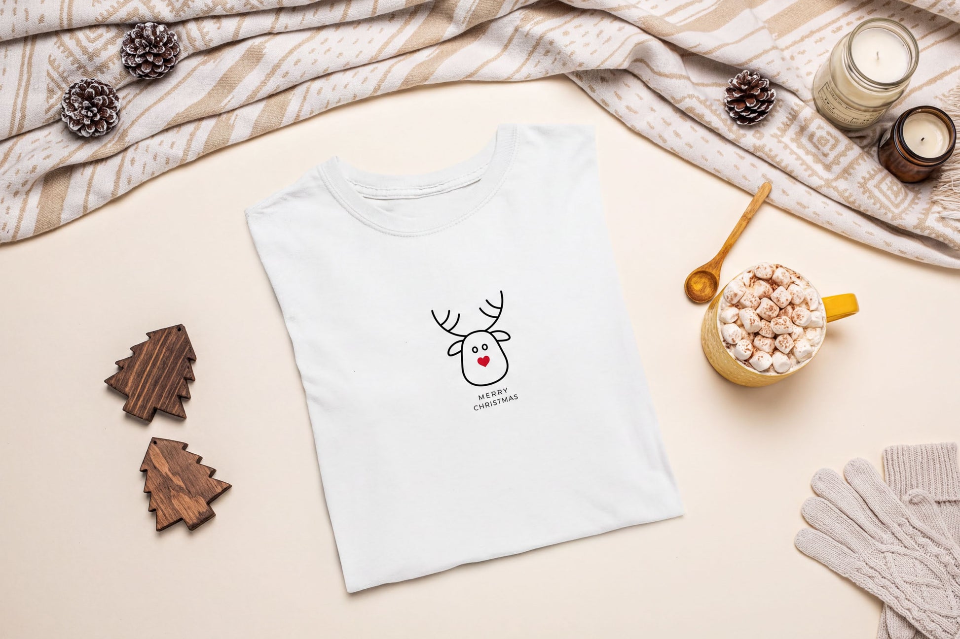 A white t-shirt with a cartoon reindeer design and the text "I love Christmas" printed on it, along with other holiday-themed items such as pine cones, a mug of hot chocolate, and a pair of gloves.