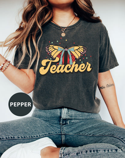 a woman wearing a teacher shirt with a butterfly on it