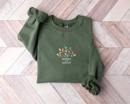 A green sweater with a Christmas-themed design and the text "MERRY BRIGHT" printed on it, laid out on a wooden surface.