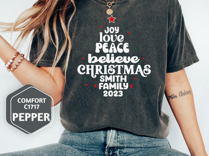 A person wearing a black t-shirt with a Christmas tree design and text printed on it, along with a necklace and bracelets.