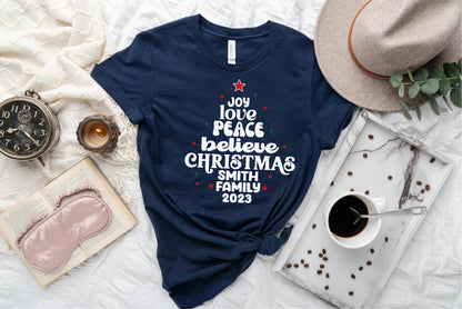 A navy blue t-shirt with a Christmas-themed design, a hat, a book, a cup of coffee, and some coffee beans on a bed.