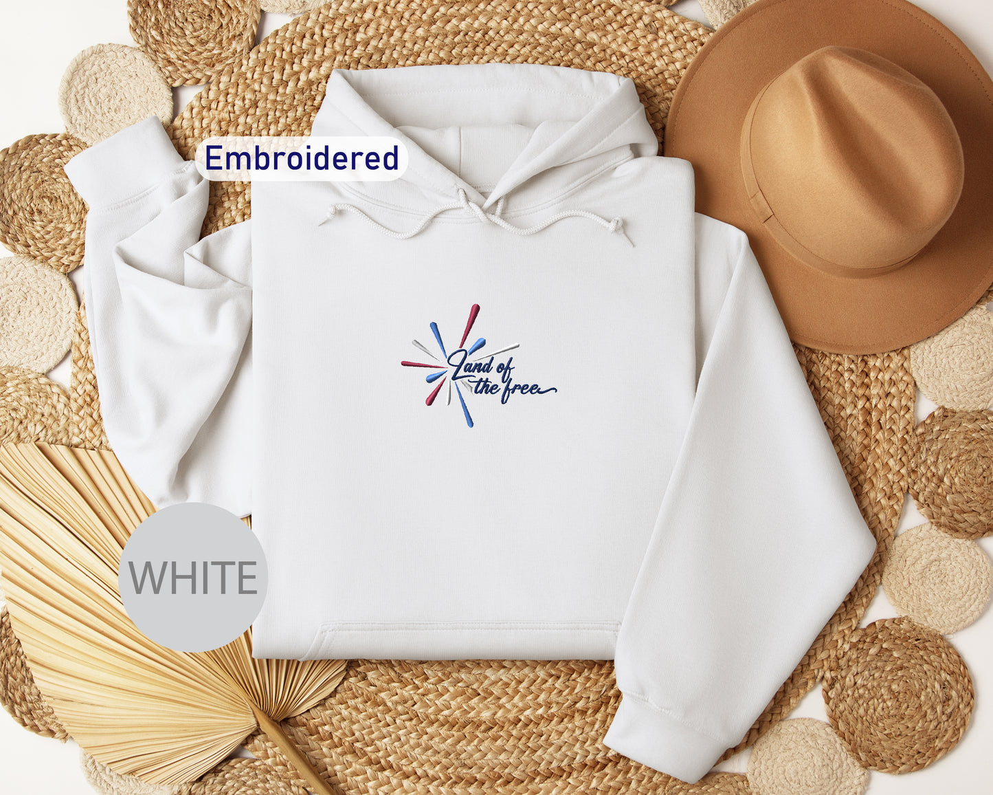a white hoodie with a graphic design, a brown hat, and some woven straw items arranged on a woven mat.