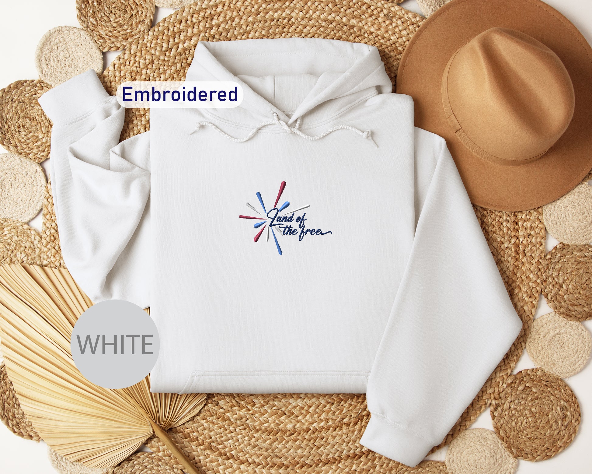 a white hoodie with a graphic design, a brown hat, and some woven straw items arranged on a woven mat.