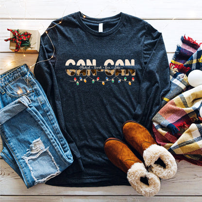 A casual outfit consisting of a black long-sleeved shirt with a graphic design, distressed blue jeans, brown boots, and a colorful plaid scarf is laid out on a wooden surface.