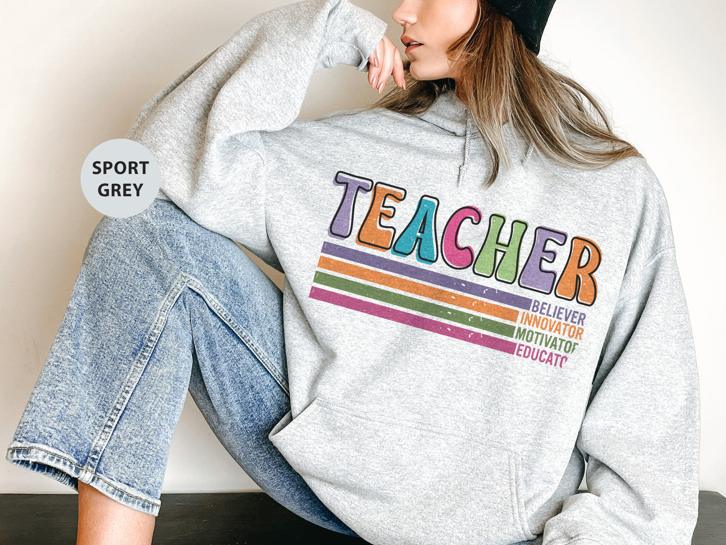 a woman sitting on the ground wearing a sweatshirt with the word teacher on it