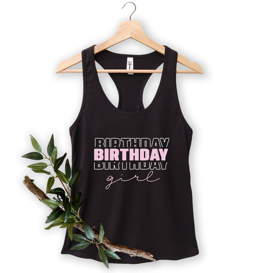 A black tank top with the text "BIRTHDAY GIRL" printed on it, hanging on a wooden hanger.