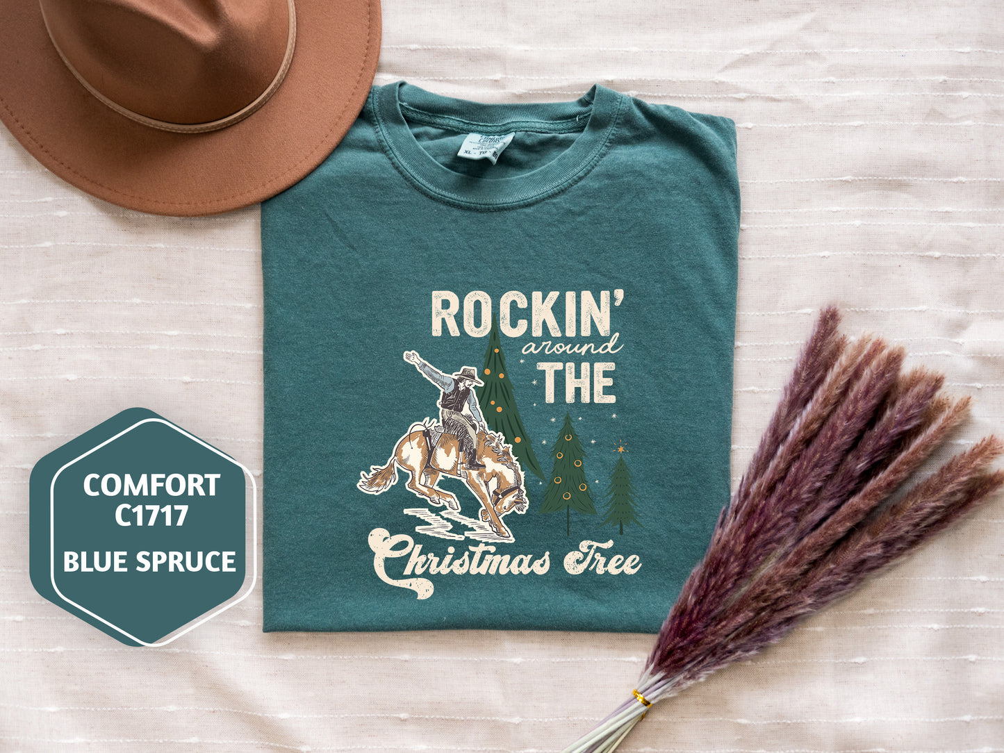 a green t-shirt with a cowboy graphic and the text "ROCKIN' around THE CHRISTMAS Tree" printed on it, along with a brown hat and some purple reeds.