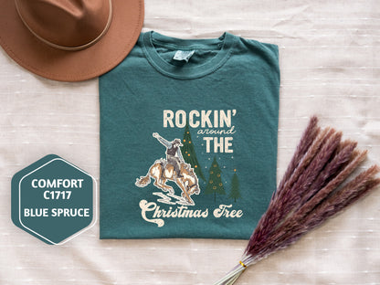 a green t-shirt with a cowboy graphic and the text "ROCKIN' around THE CHRISTMAS Tree" printed on it, along with a brown hat and some purple reeds.