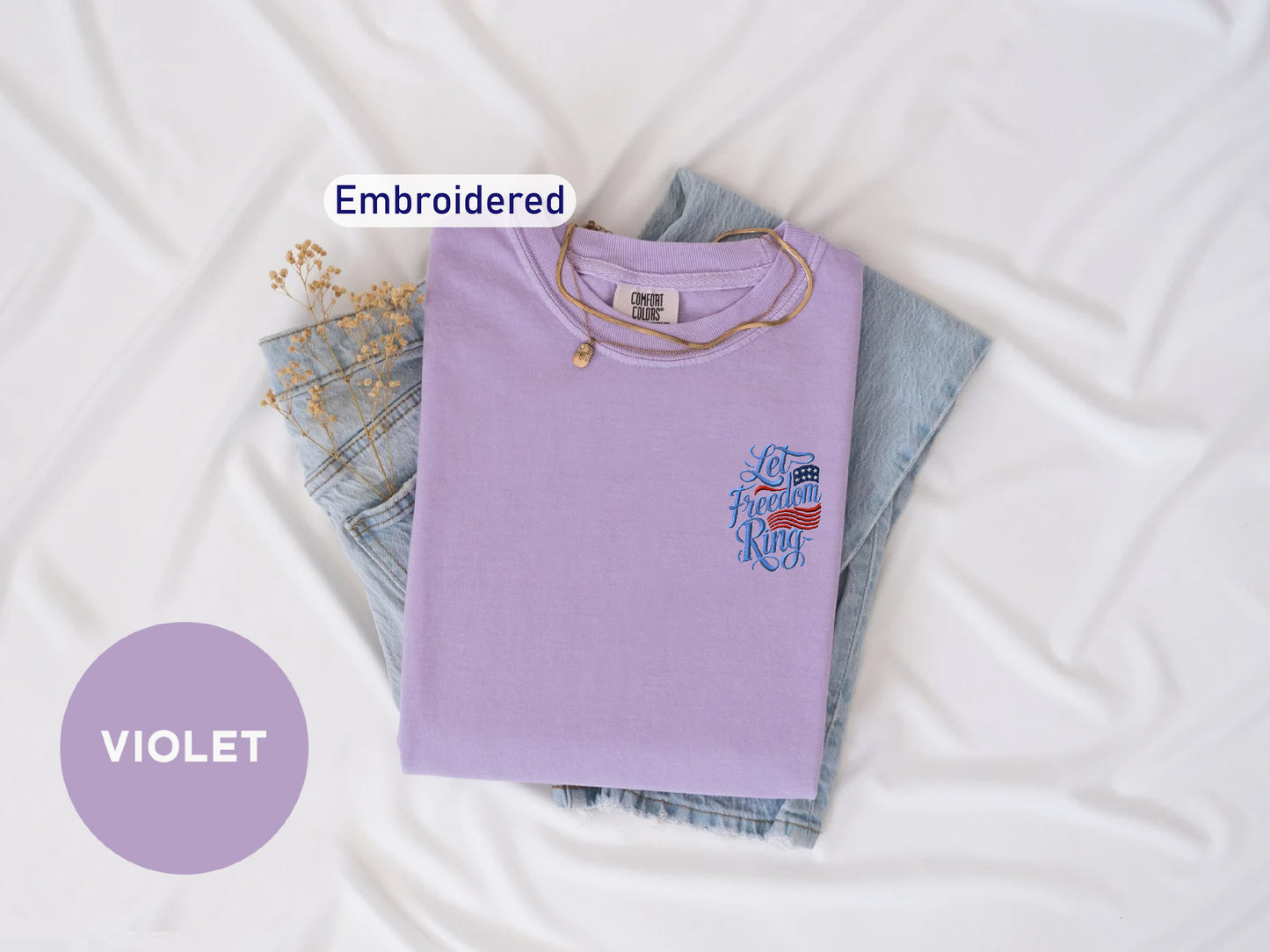 a purple t-shirt with a design, a pair of denim jeans, and a necklace, all laid out on a white background.