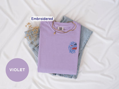 a purple t-shirt with a design, a pair of denim jeans, and a necklace, all laid out on a white background.