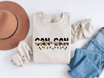 A beige sweatshirt with the text "CAN CAN" printed on it, along with a brown hat and blue jeans, are laid out on a white background.