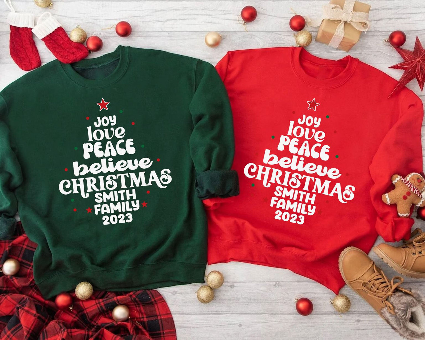 two Christmas-themed sweatshirts with the text "Joy love peace believe christmas Smith family 2020" printed on them, along with a pair of red and green plaid socks and a pair of brown boots. The sweatshirts are placed on a white surface, surrounded by Christmas decorations such as ornaments, a gift box, and a star.