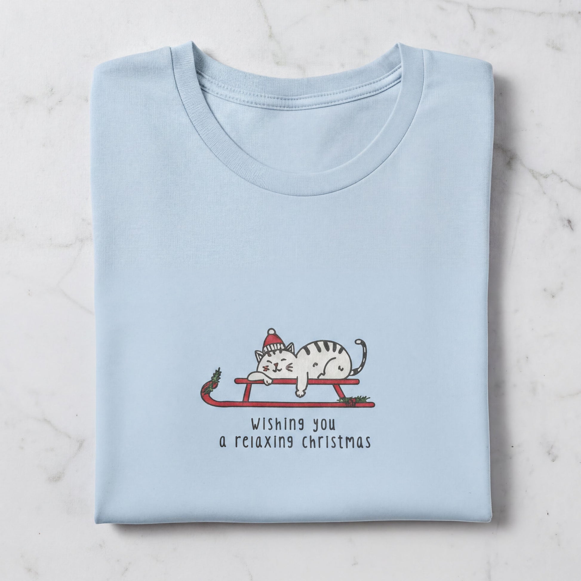 A light blue t-shirt with a graphic design depicting a cat wearing a Santa hat and riding a sled, along with the text "Wishing you a relaxing christmas".