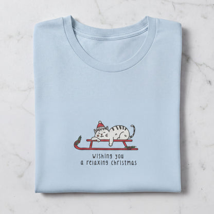 A light blue t-shirt with a graphic design depicting a cat wearing a Santa hat and riding a sled, along with the text "Wishing you a relaxing christmas".