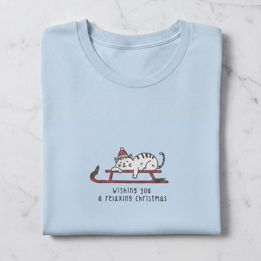A light blue t-shirt with a graphic design depicting a cat wearing a Santa hat and riding a sled, along with the text "Wishing you a relaxing christmas".