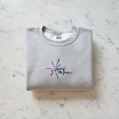 A gray sweatshirt with a red, white, and blue embroidered design on the front, along with the text "Land of the free" printed on it.