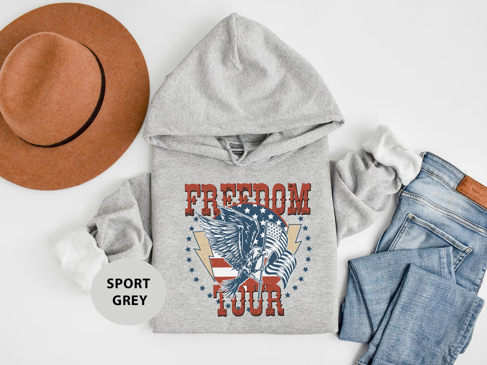 A gray hoodie with a graphic design, a brown hat, a pair of jeans, and a gray sweatshirt with the text "FREEDOM TOUR" printed on it, all laid out on a white background.
