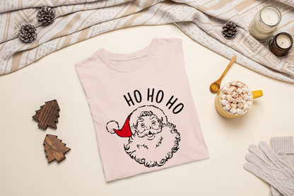 a pink t-shirt with a Santa Claus design, a mug of hot chocolate, pine cones, and a pair of gloves, all arranged on a beige background.