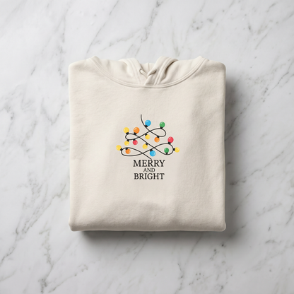 A beige hoodie with a graphic design of colorful Christmas lights and the text "MERRY AND BRIGHT" printed on it.