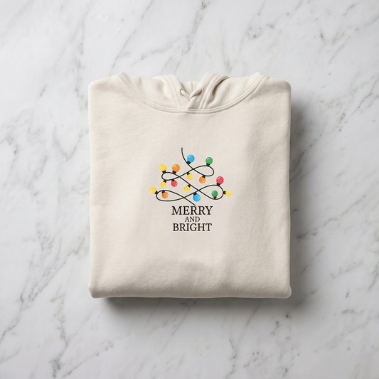 A beige hoodie with a graphic design of colorful Christmas lights and the text "MERRY AND BRIGHT" printed on it.