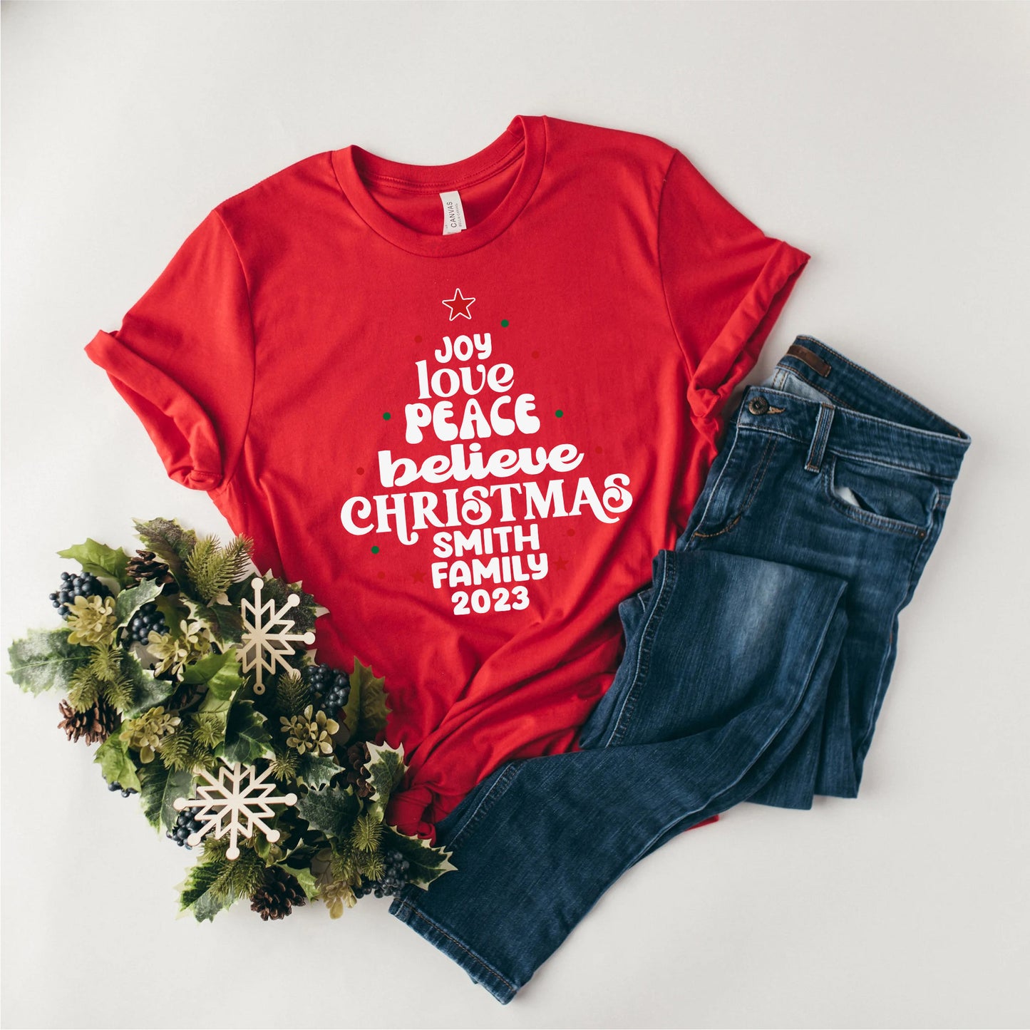 A red t-shirt with white text and a Christmas wreath are displayed on a white background.