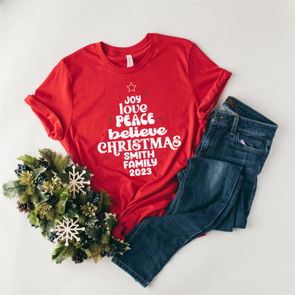 A red t-shirt with white text and a Christmas wreath are displayed on a white background.
