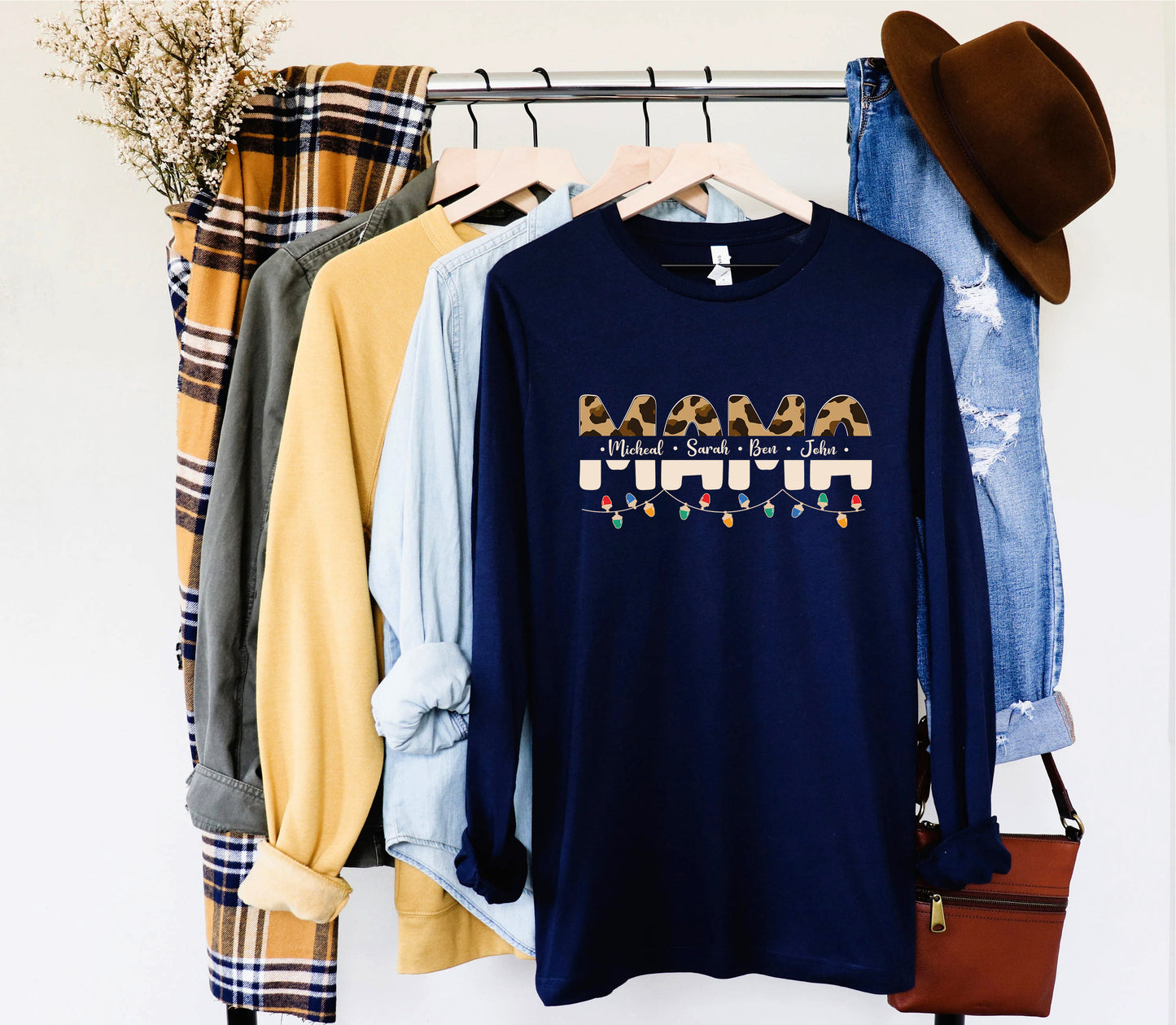 A collection of clothing items, including a navy blue long-sleeved shirt with a graphic design, a plaid shirt, a yellow shirt, and a pair of blue jeans, are hanging on a clothing rack.