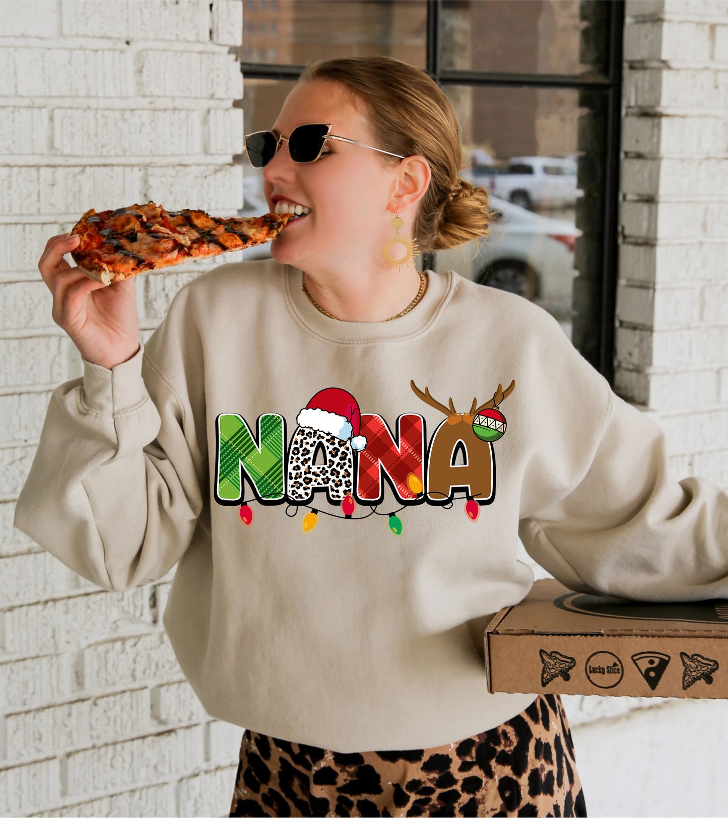 A woman wearing a sweater with the word "NANA" on it is eating a slice of pizza.