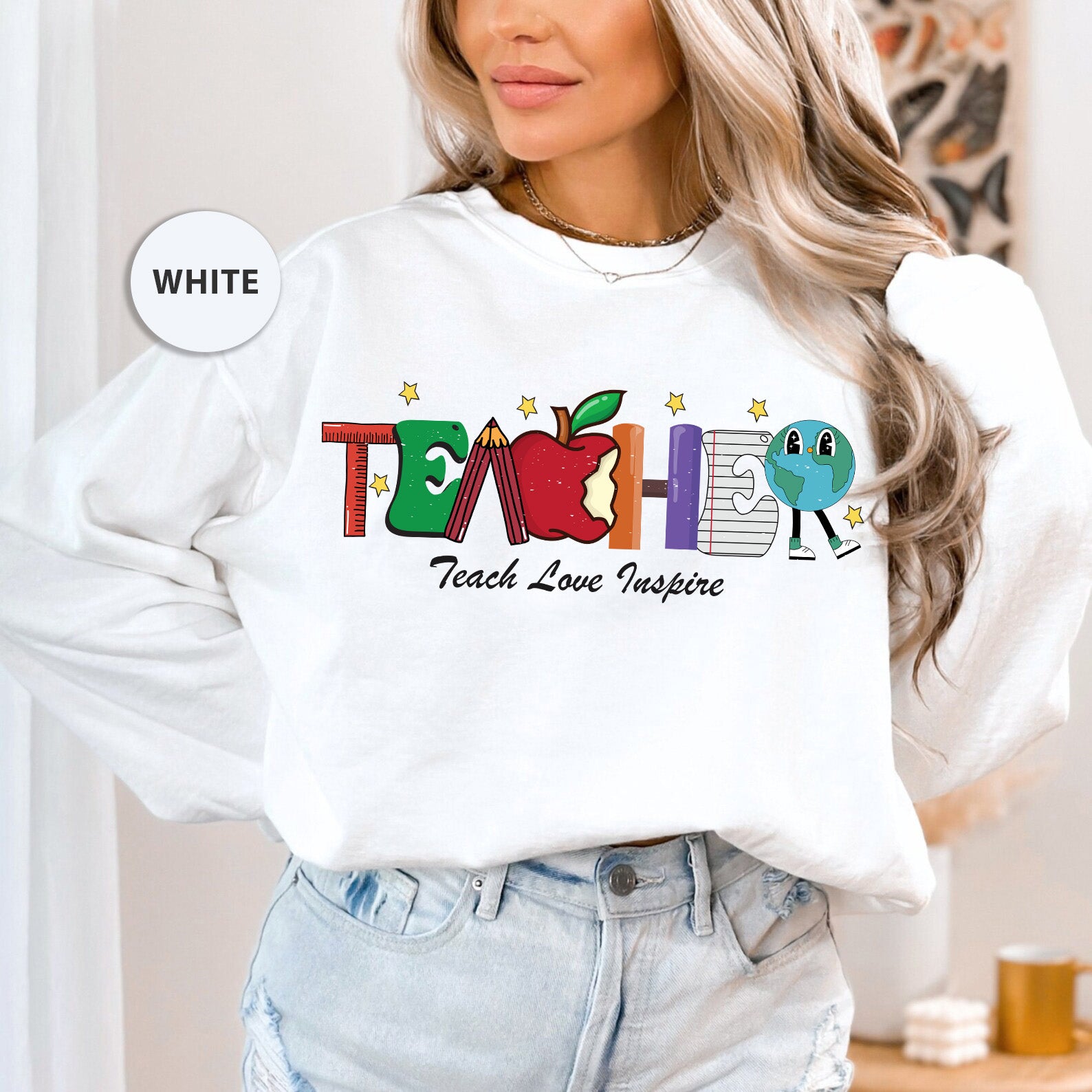 a woman wearing a white teacher sweatshirt and jeans