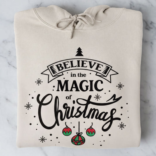 A beige hoodie with a printed design that says "Believe in the Magic of Christmas" and includes Christmas-themed elements such as snowflakes and ornaments.