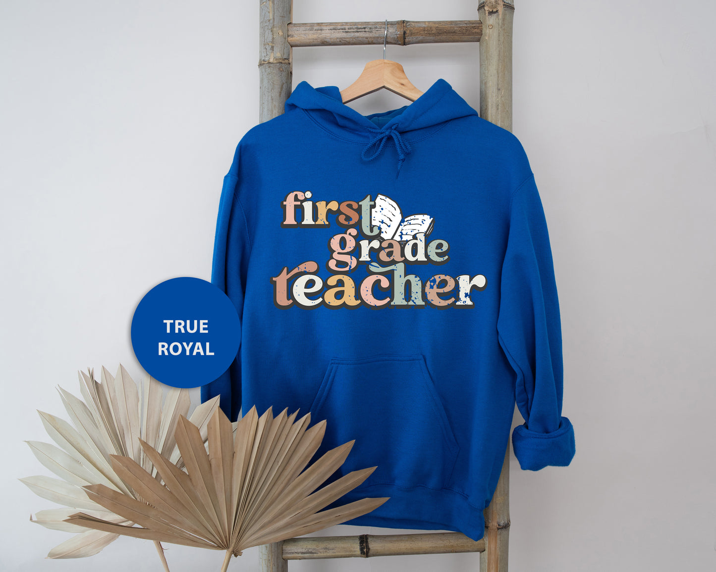 A blue hoodie with the text "first grade teacher" printed on it, hanging on a wooden ladder.