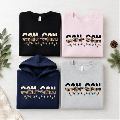 four t-shirts with the text "CAN CON" printed on them, along with a hoodie and a gray sweatshirt. The t-shirts are arranged in a grid-like pattern on a white background, with a pine branch and greenery visible in the top right corner.
