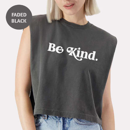 a woman with blonde hair wearing a black crop top that says be kind